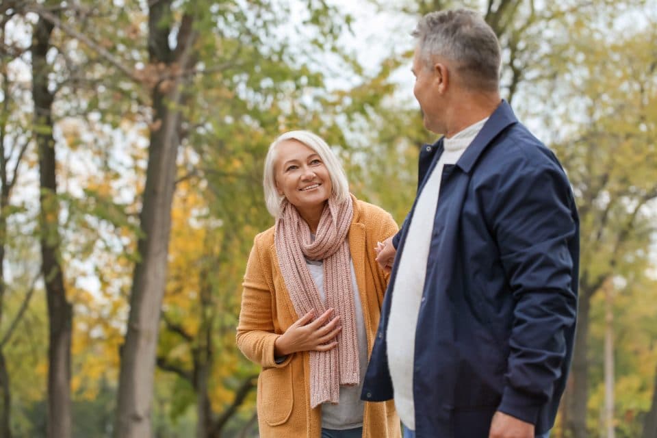 An older couple walking arm in arm outdoors among autumn trees